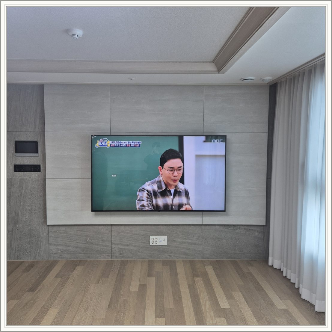 거실 회색 패널과 벽걸이 TV / TV 아래 콘센트와 양쪽 마감 판넬의 대비가 뚜렷합니다
