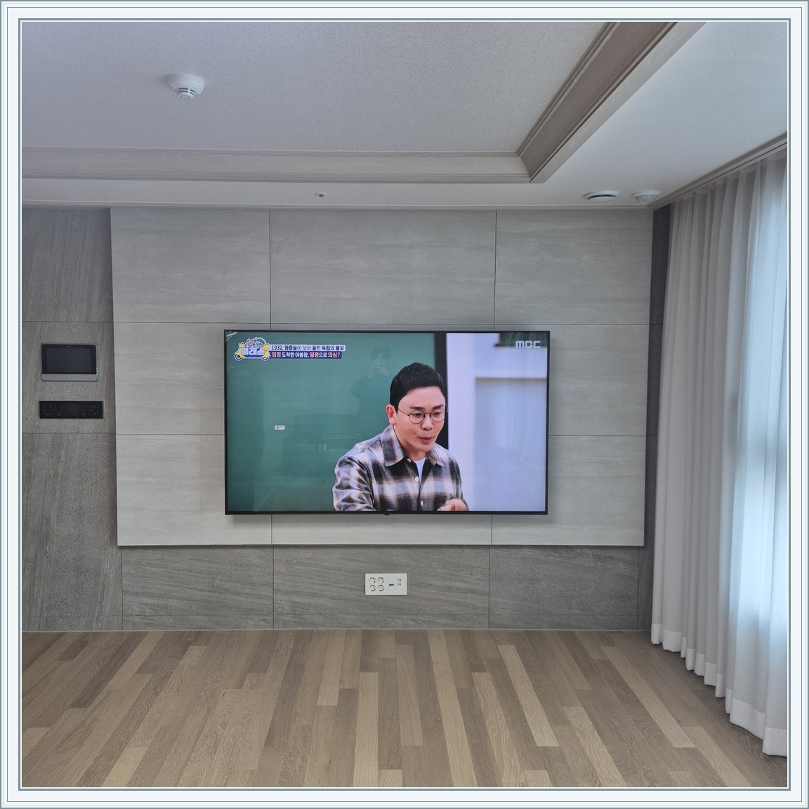 거실 회색 패널과 벽걸이 TV / TV 아래 콘센트와 양쪽 마감 판넬의 대비가 뚜렷합니다