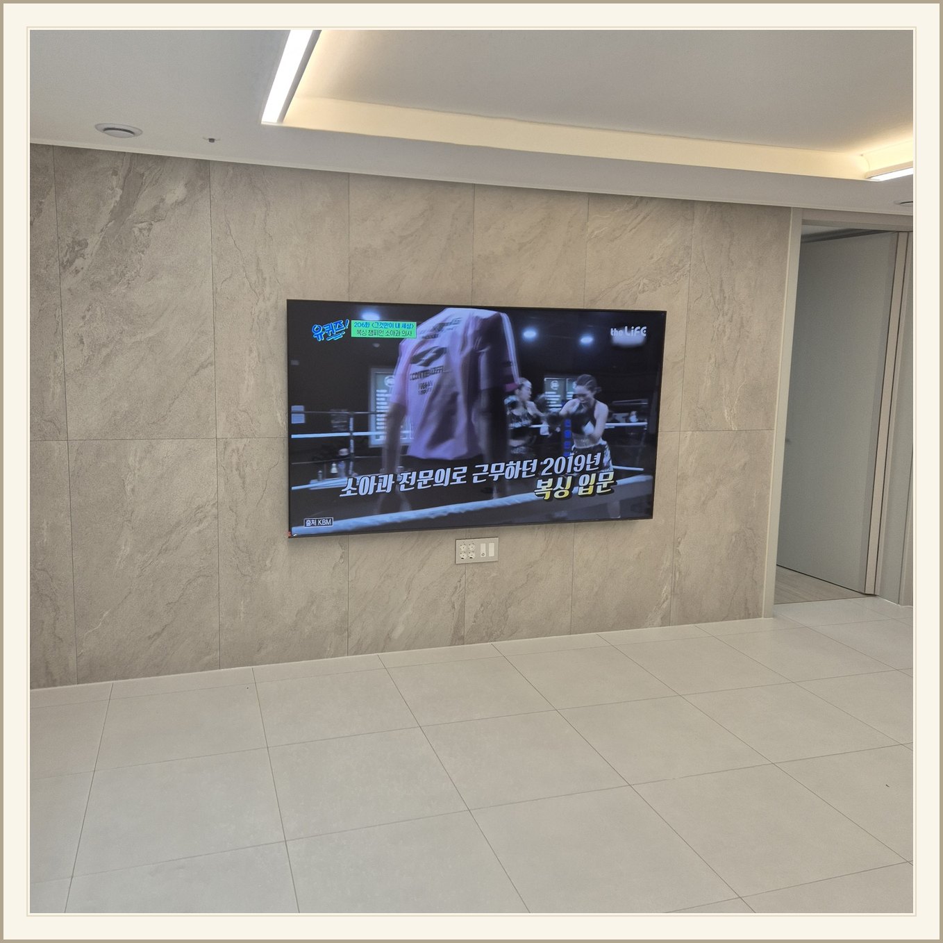 석재 느낌 벽면을 정면에서 본 TV / 넓은 바닥 여유와 조명 라인이 동시에 보입니다