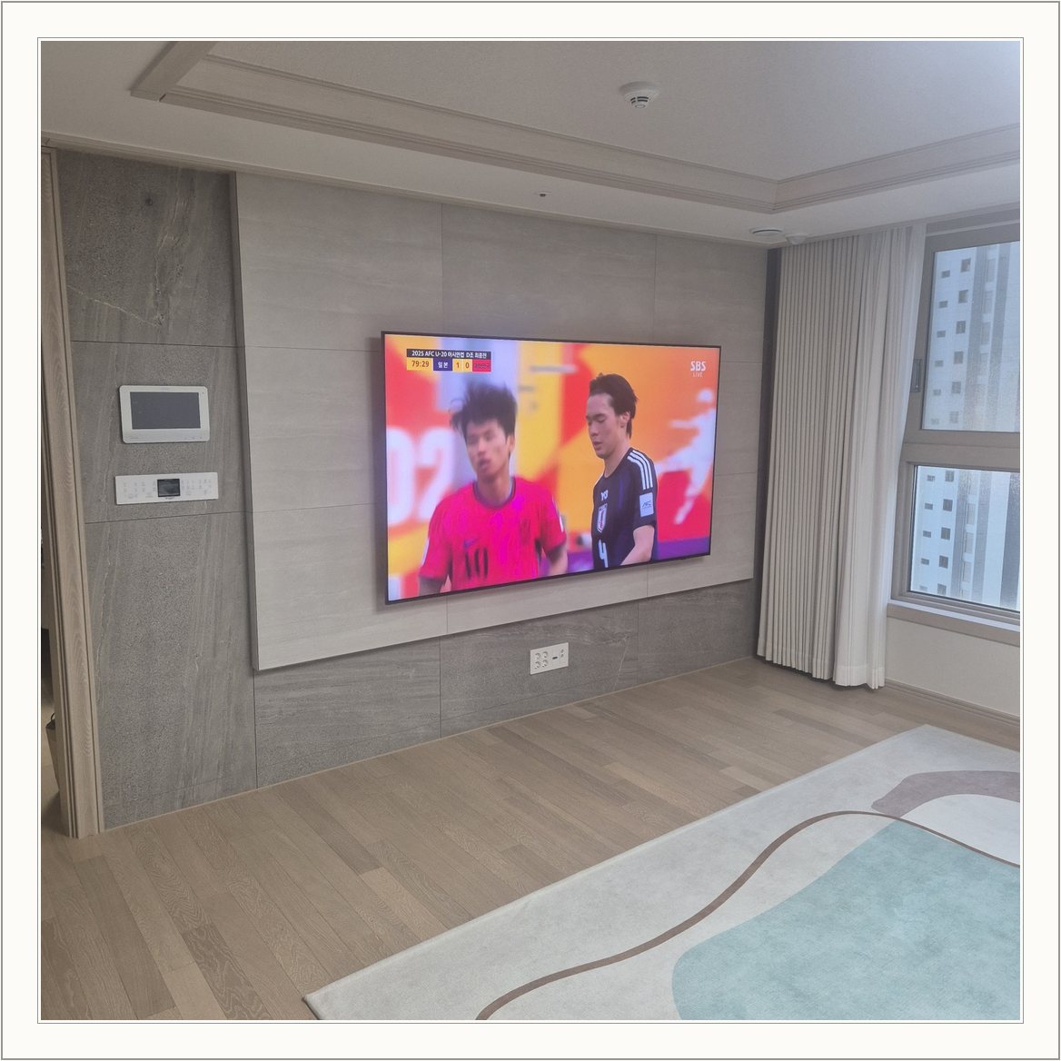 밝은 회색 아트월과 시청 공간 / 밝은 몰딩과 TV 아래 전원 위치가 같이 나타납니다