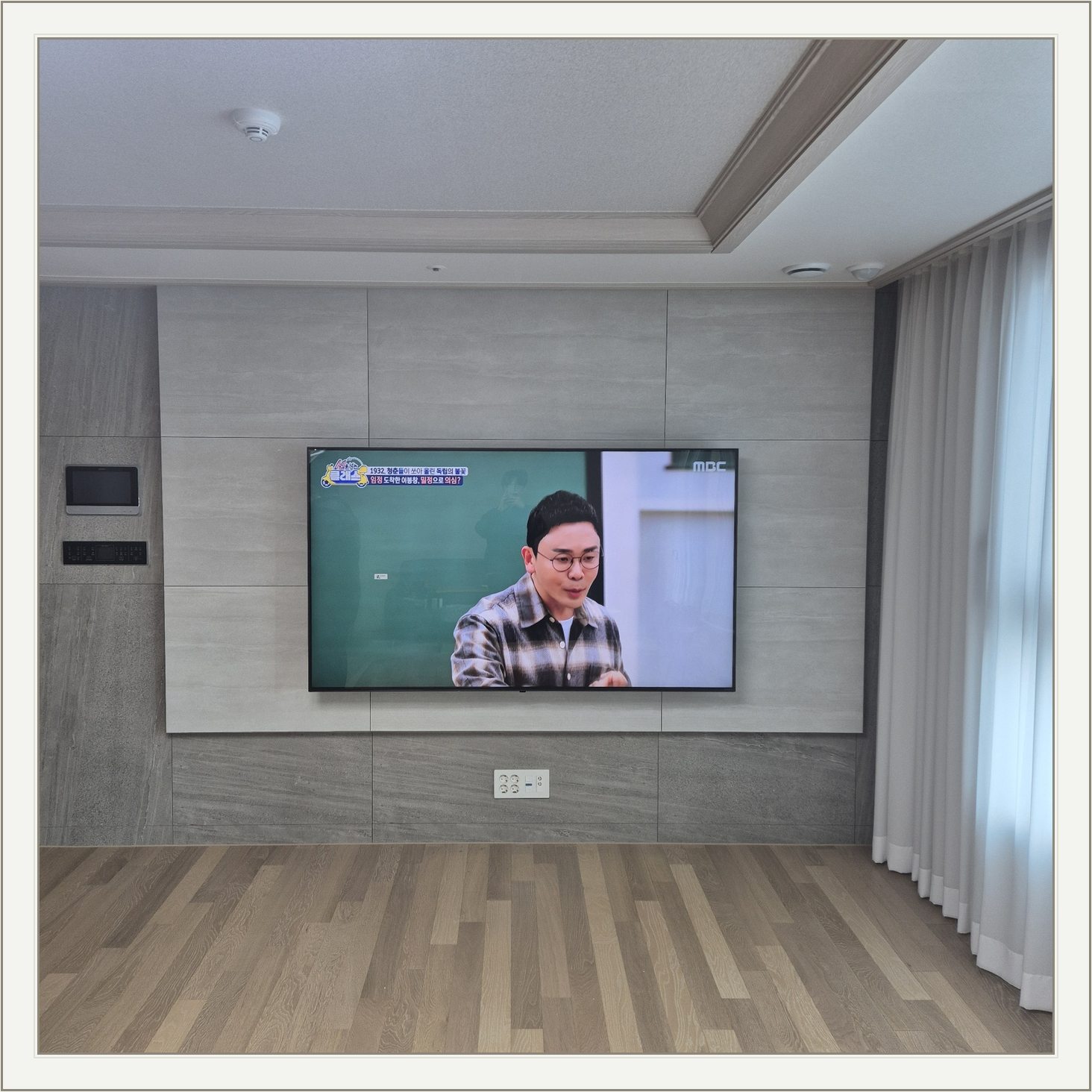 거실 회색 패널과 벽걸이 TV / TV 아래 콘센트와 양쪽 마감 판넬의 대비가 뚜렷합니다