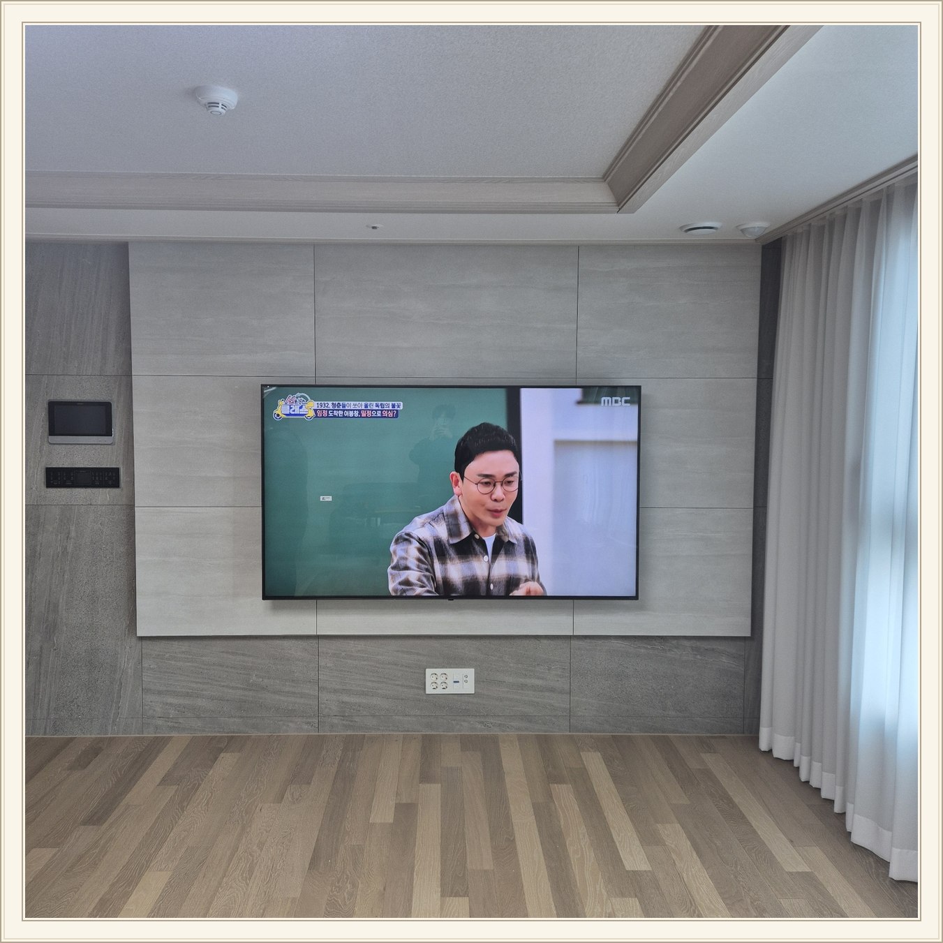 거실 회색 패널과 벽걸이 TV / 오른쪽 커튼 옆으로 화면이 중심에 놓여 있습니다